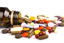 A brown medicine bottle on its side with a range of colourful pills and tablets spilled out.
