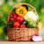 A wicker basket of brightly coloured leafy green vegetables and tomates.