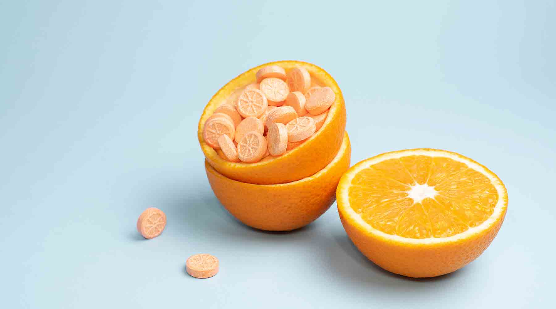 An orange cut in half and full of tablets on a white backgound.