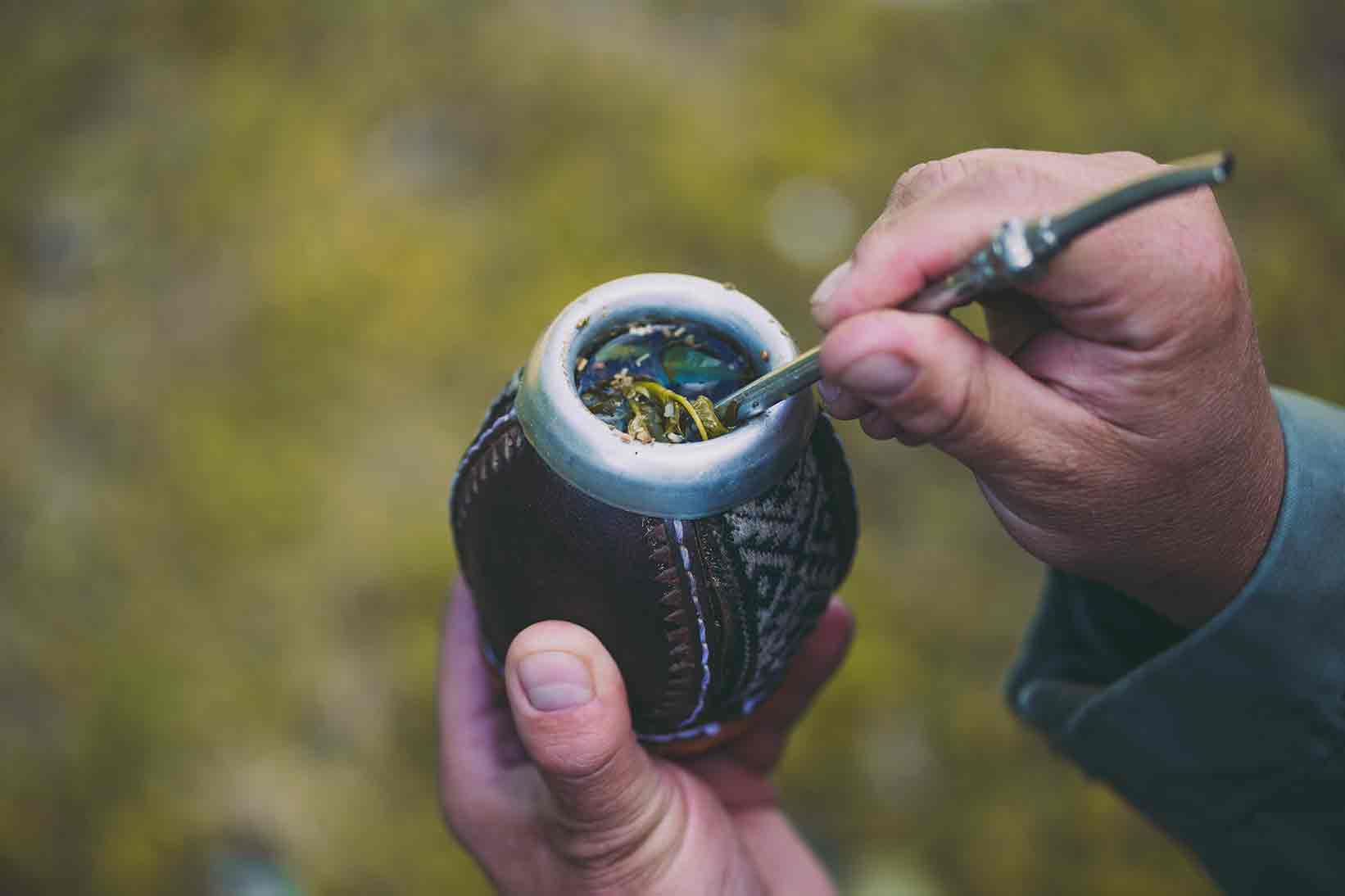 Old man holding a yerba mate gourd and bombilla outside in nature.